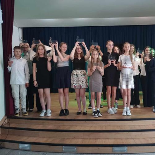 Zdjęcie grupowe uczniów cyklu sześcioletniego. Uczniowie są zadowoleni. Trzymają w dłoniach statuetki z kluczem wiolinowym