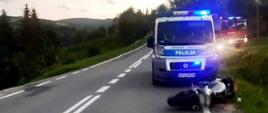 Motocykl leży przed radiowozem na skraju drogi.