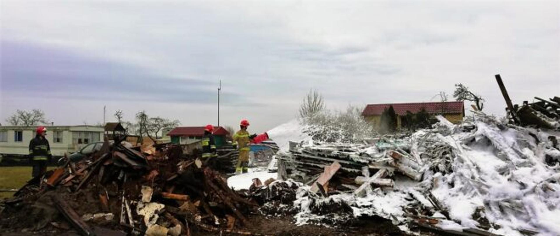 Zdjęcie przedstawia strażaków dogaszających pozostałości po pożarze stodoły. 