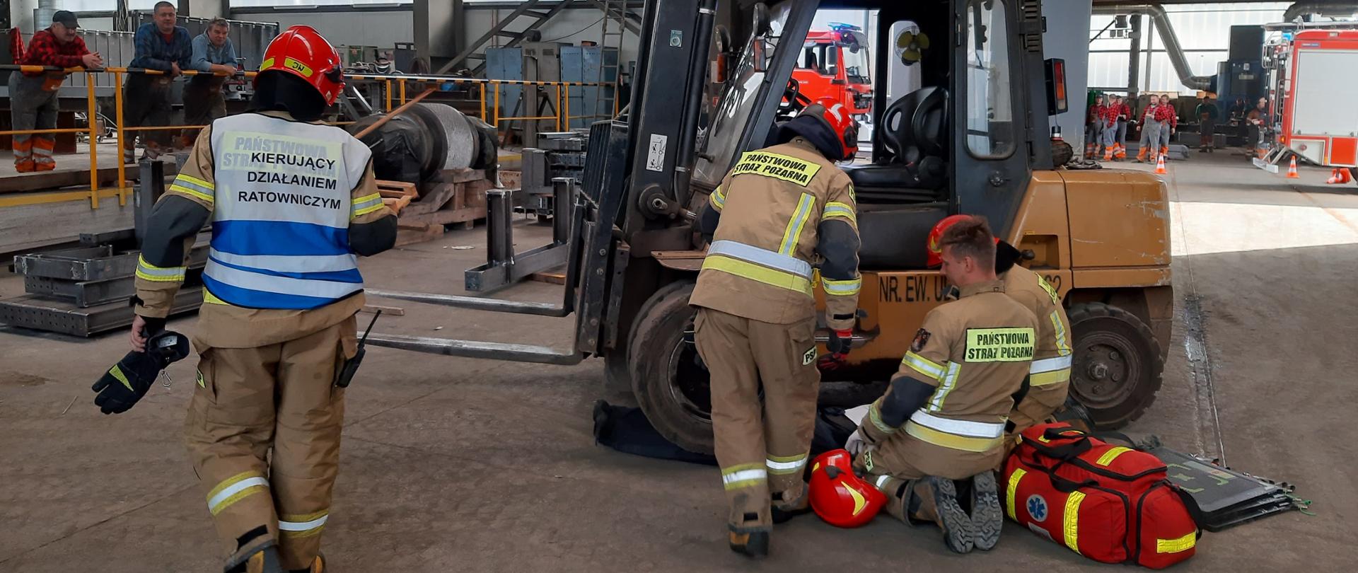 Zdjęcie przedstawia uwalnianie osoby przyciśniętej przez wózek widłowy przez strażaków przy użyciu poduszek pneumatycznych