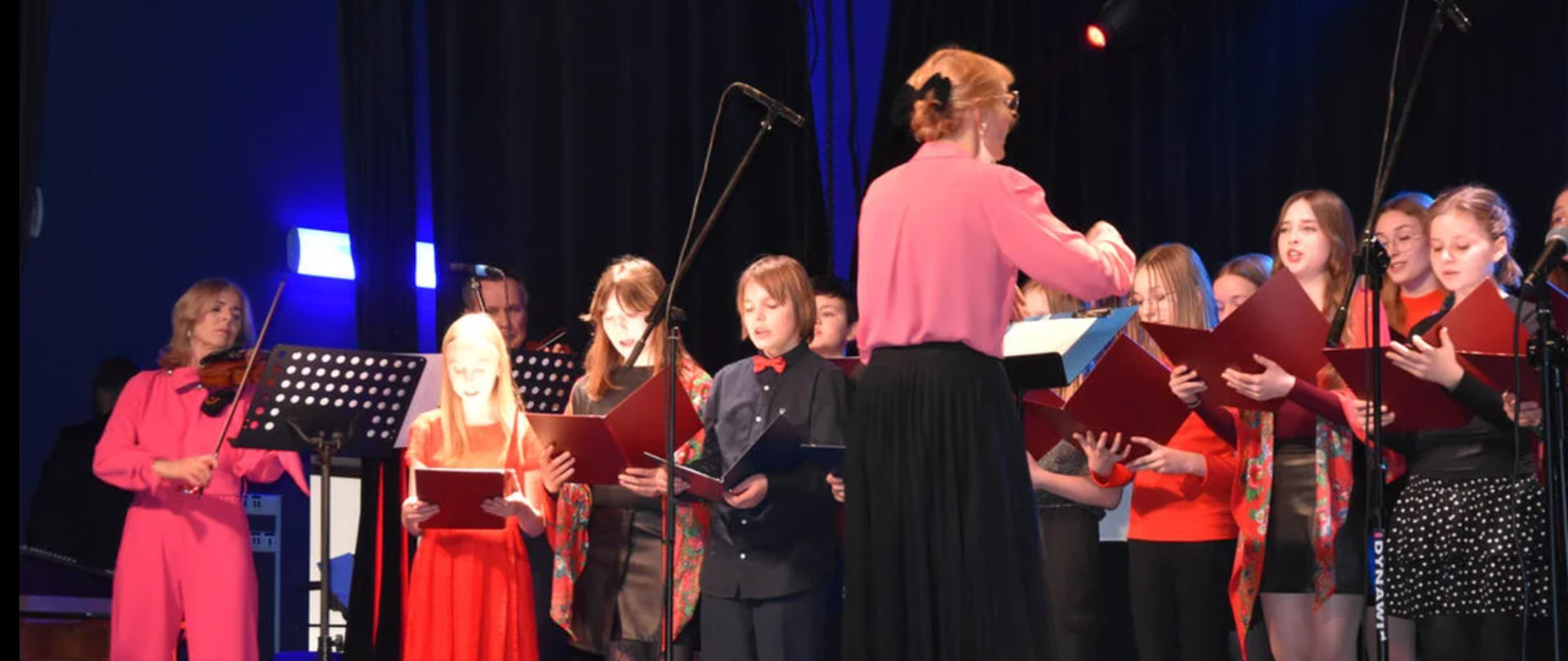 Zdjęcie przedstawia chór szkolny wystepujący na scenie GOK Hutnik. 