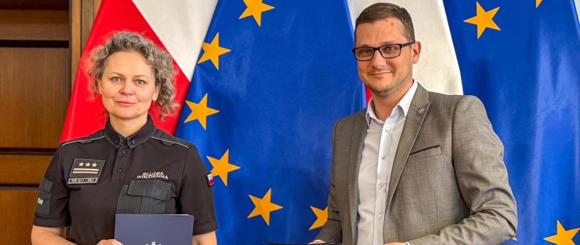 Płk Marta Jakubowska, Dyrektor Okręgowy Służby Więziennej w Bydgoszczy, stoi obok Wojewody Kujawsko-Pomorskiego Michała Sztybla na tle flagi RP i UE