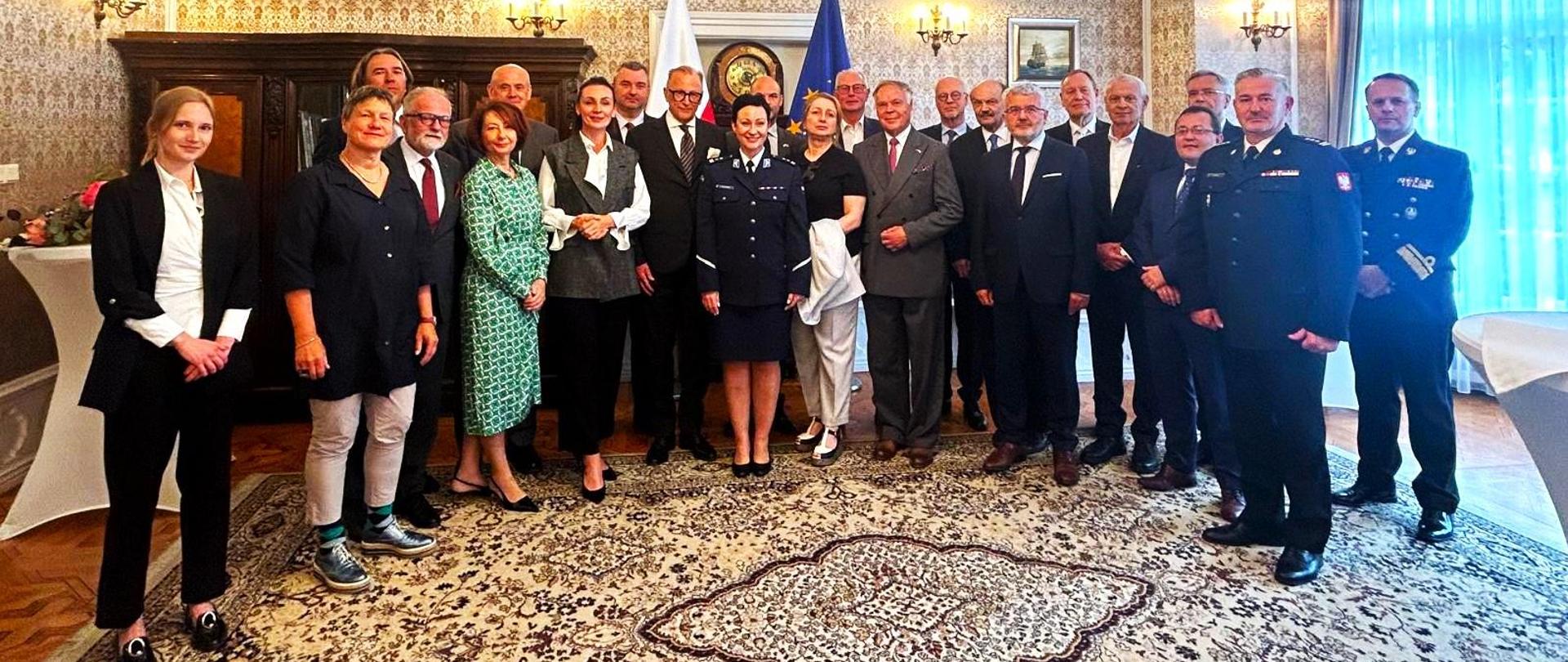 grupa osób stoi w sali pozując do zdjęcia, w tle flagi polska i unijna