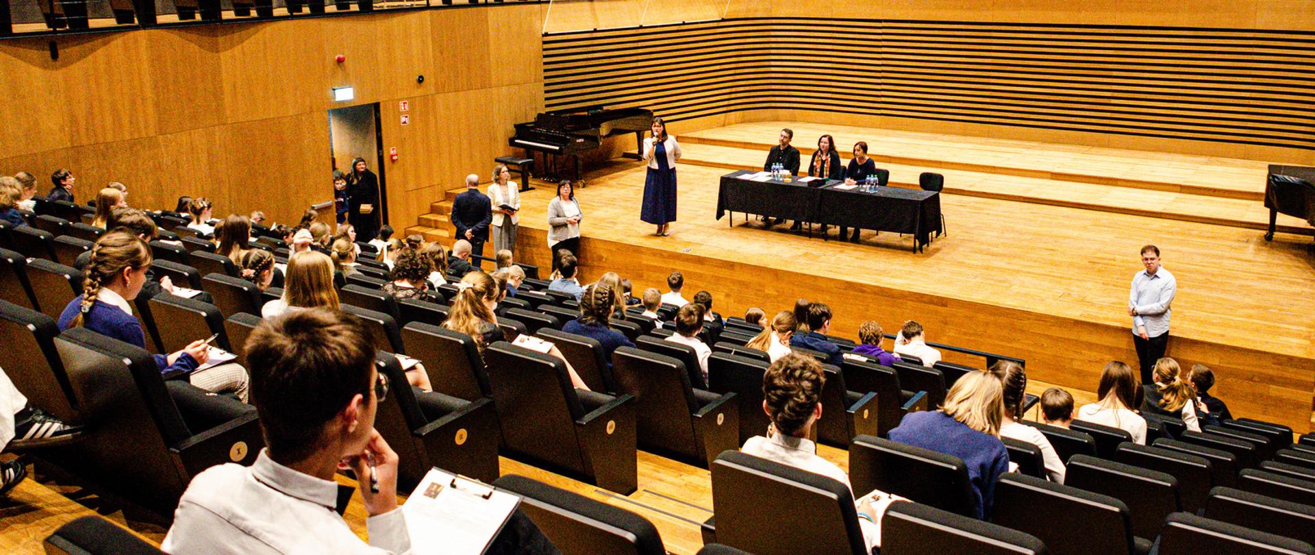 Zdjęcie przedstawia uczniów i jury siedzących na sali koncertowej