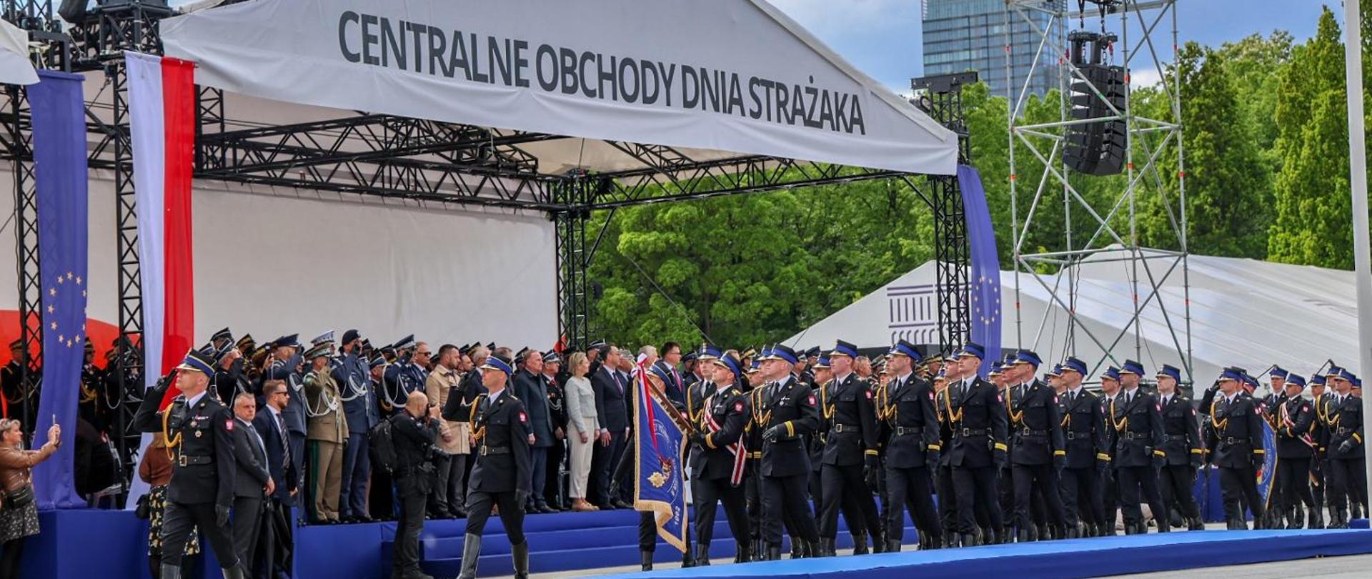 Trybuna honorowa oraz defilujące przed nią pododdziały.