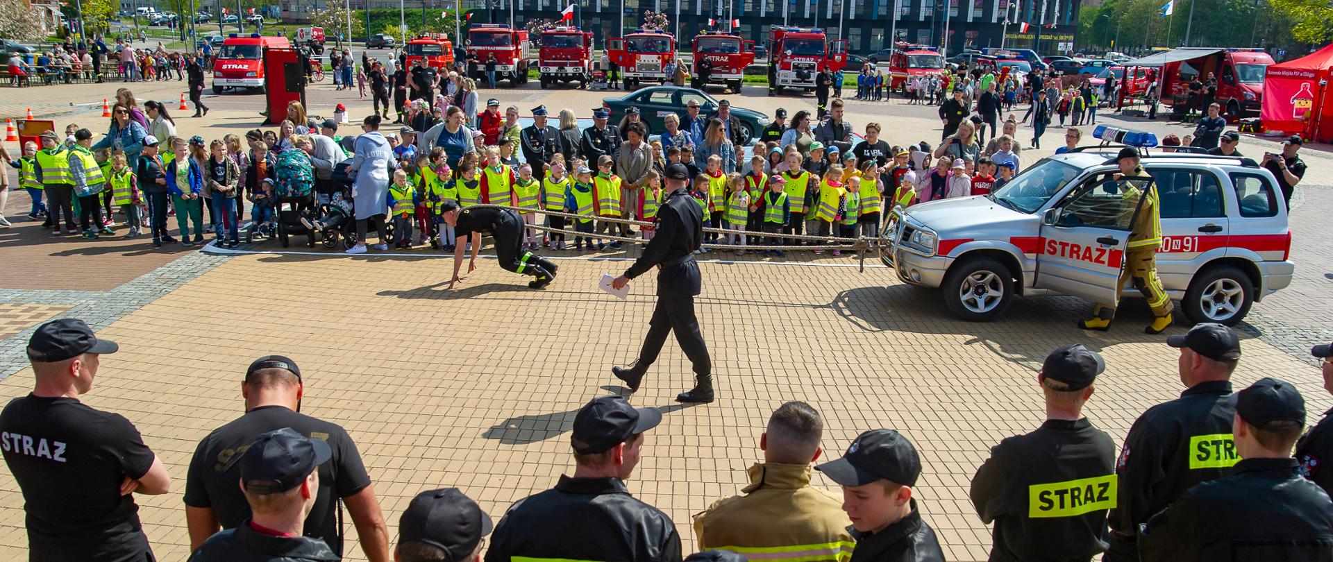 Plac Kazimierza Jagiellończyka w Elblągu wypełniony mieszkańcami miasta oraz strażakami. W tle pojazdy pożarnicze.