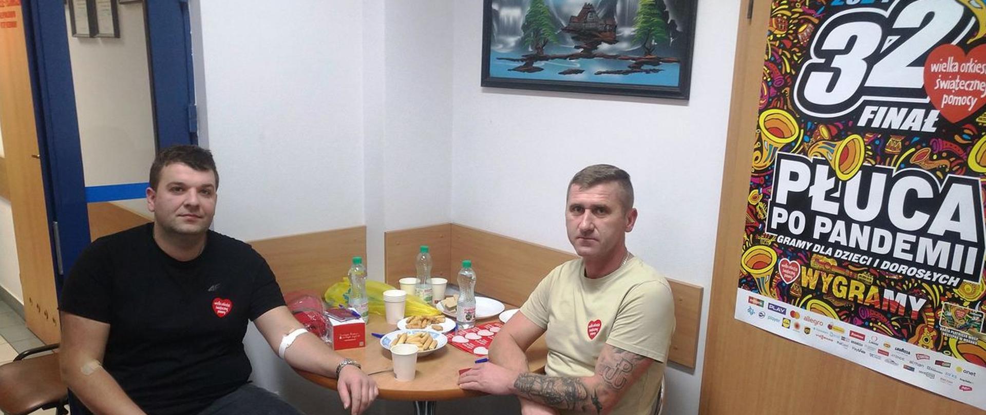 Osoby siedzą przy stole na piersiach maja naklejone serduszka