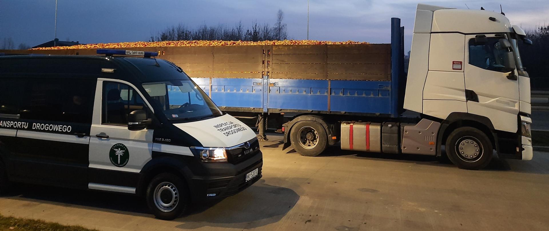 Na pierwszym planie (od lewej): oznakowany furgon mazowieckiej Inspekcji Transportu Drogowego. W tle: ciągnik siodłowy z podpiętą naczepą. Na naczepie są przewożone jabłka luzem. Owoce wystają poza podwyższone burty naczepy.