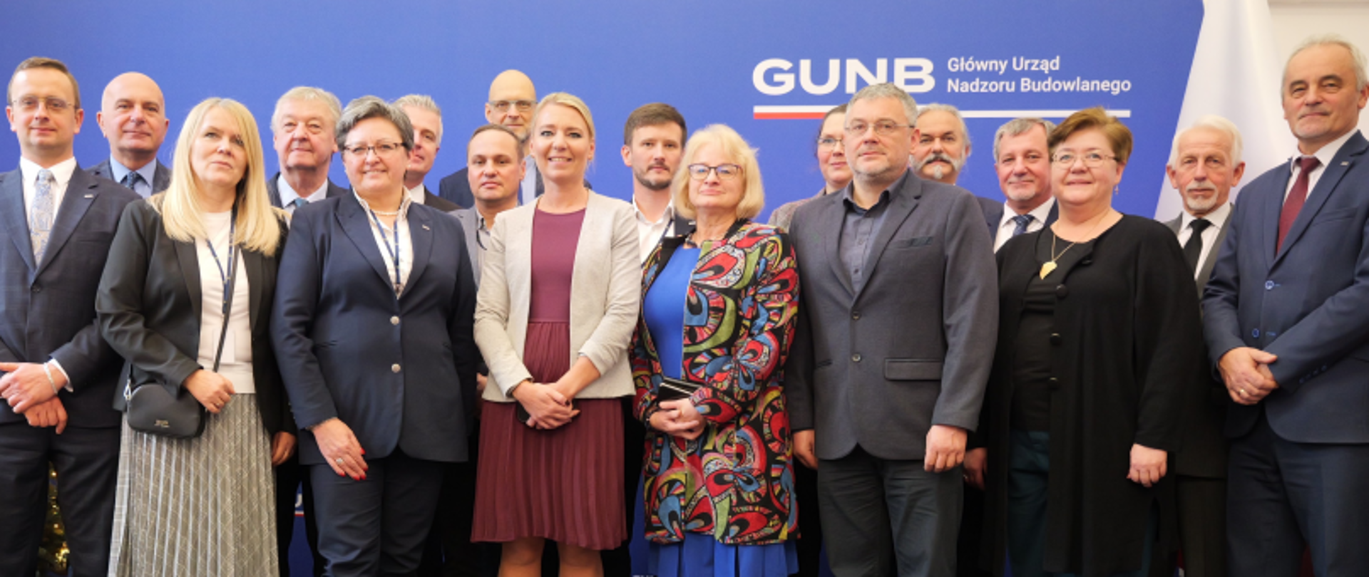 Grupa osób stojąca przed niebieską ścianką z napisem „GUNB Główny Urząd Nadzoru Budowlanego”, obok choinka bożonarodzeniowa.