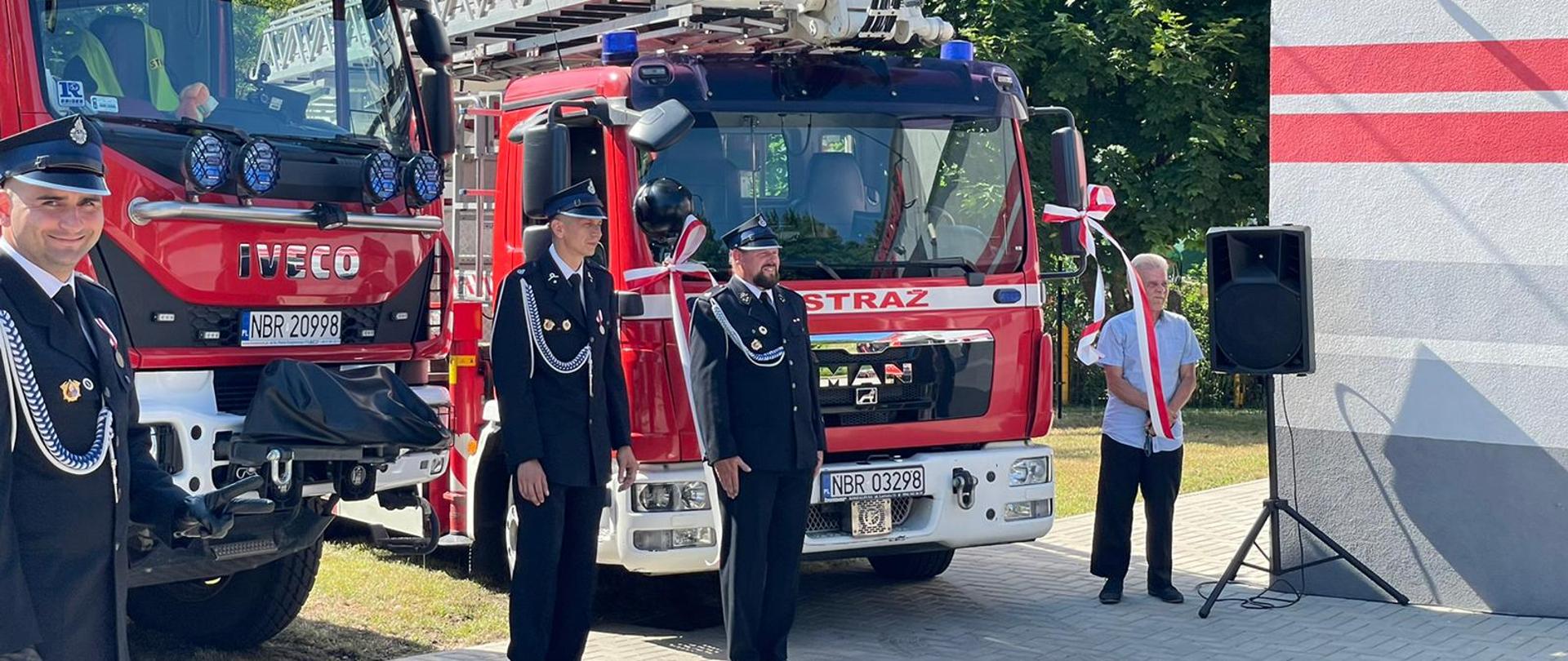 Strażacy w mundurach galowych przy samochodach strażackich