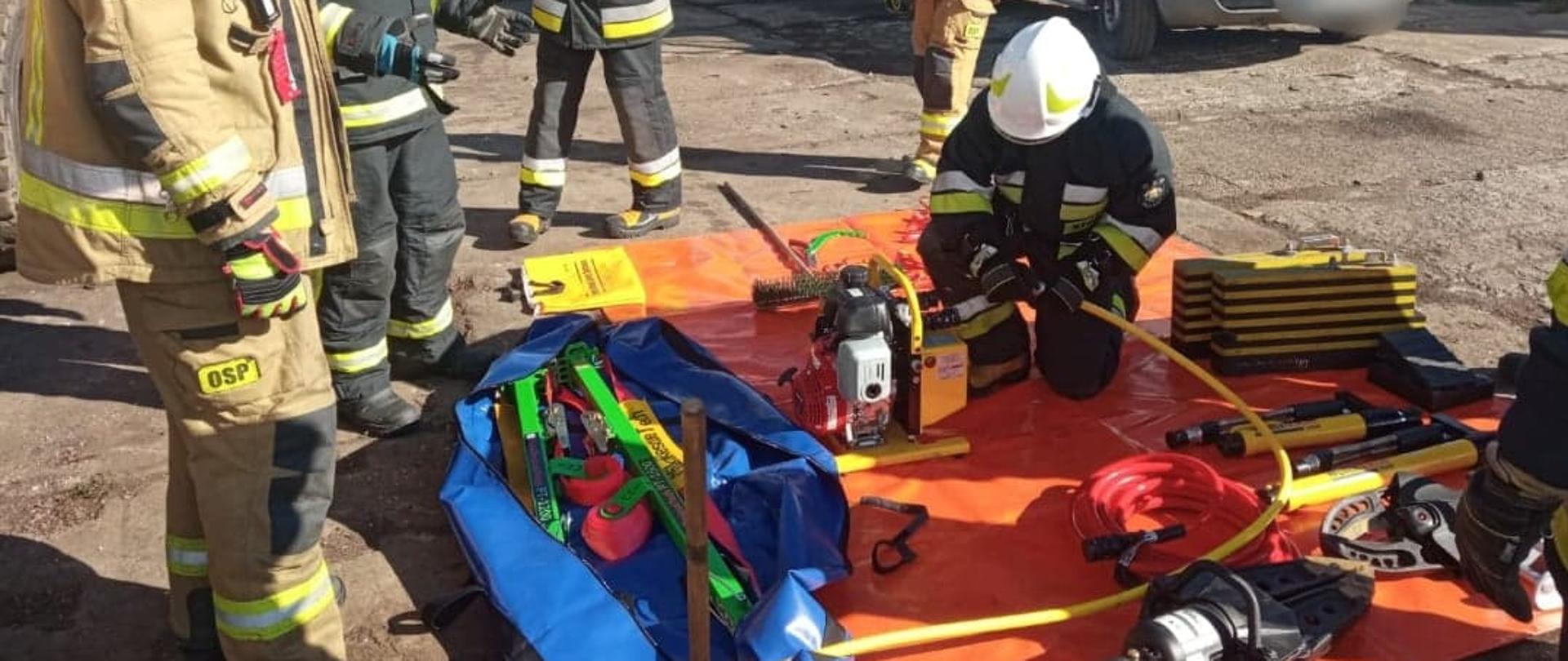 Zdjęcie przedstawia grupę strażaków, podczas zapoznania ze specjalistycznym sprzętem wykorzystywanym podczas wypadków drogowych przez Straż Pożarną.