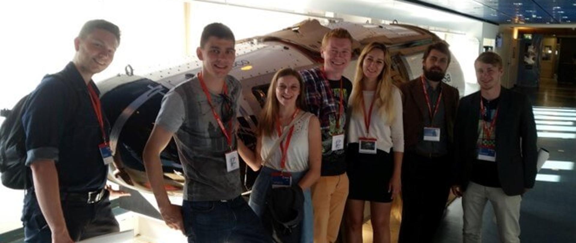 Grupa studentów na tle białej, podłużnej maszyny