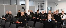 Strażacy siedzą na krzesłach ubrani w mundury służbowe lub sztabowe.