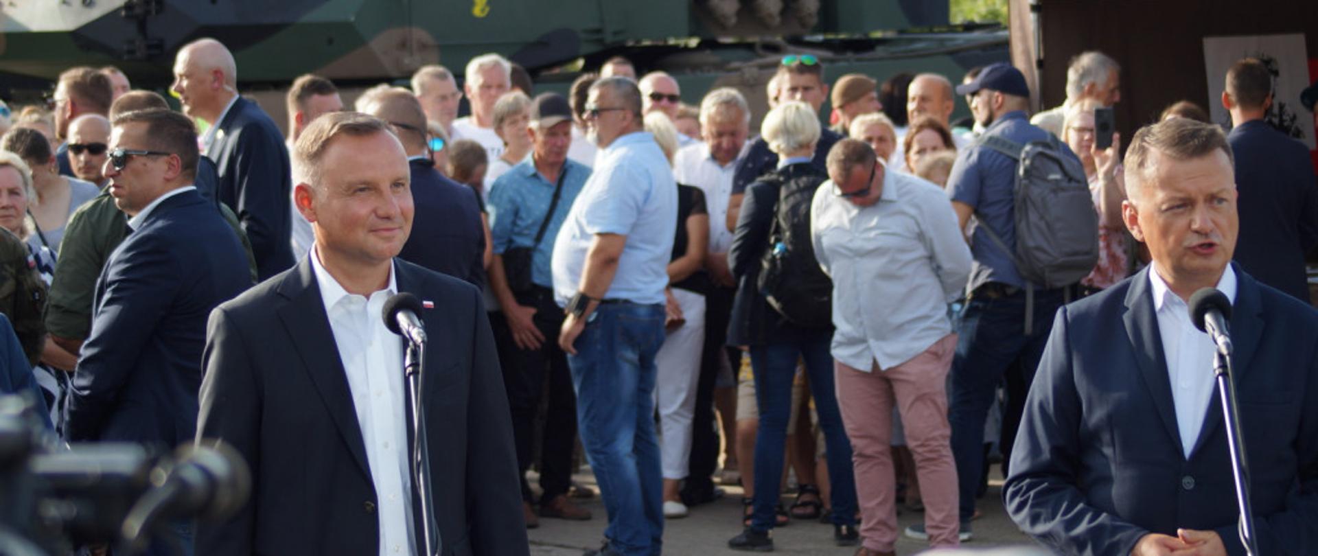 Na zdjęciu widoczny Prezydent RP Andrzej Duda wraz z Ministrem Obrony Narodowej Mariuszem Błaszczakiem. W tle zwiedzający piknik oraz sprzęt wojskowy.