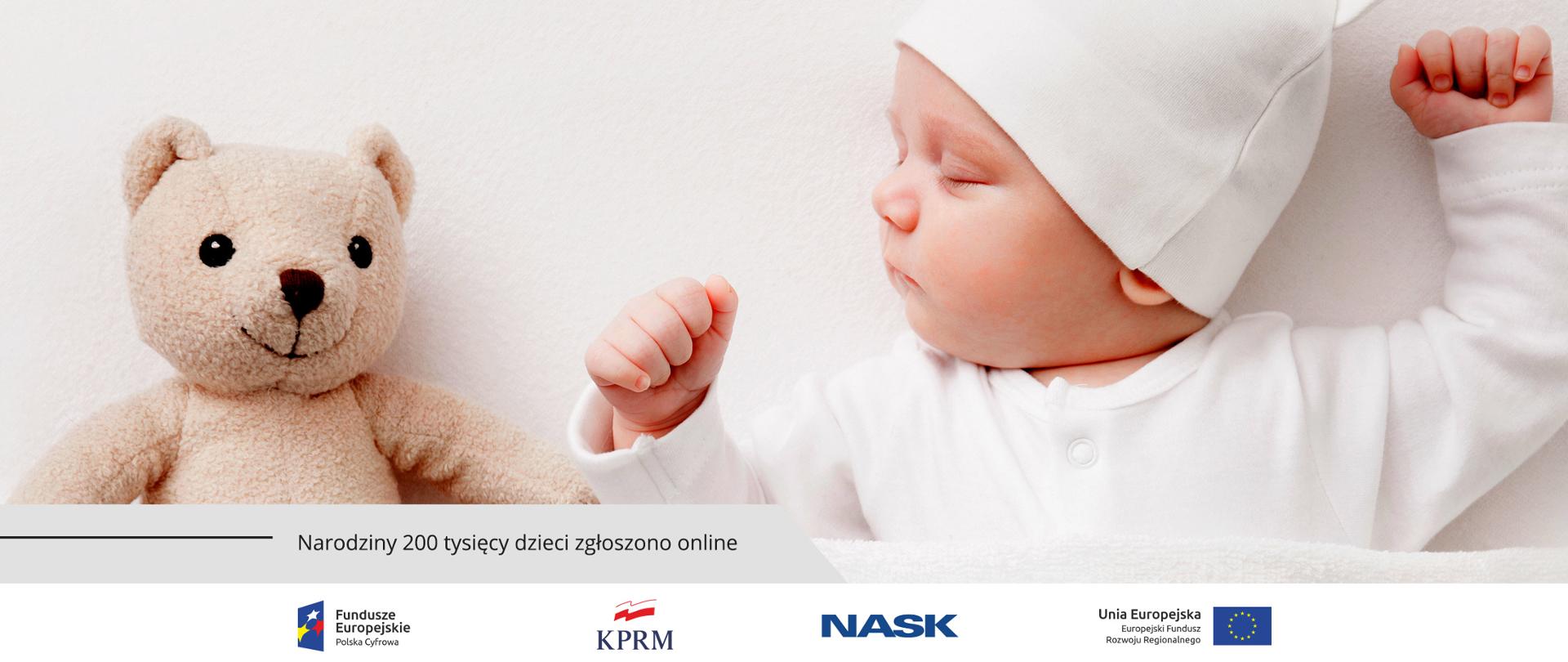 Śpiące, ubrane na biało niemowlę. Z jego prawej strony - maskotka miś. Na dole tekst: Narodziny 200 tysięcy dzieci zgłoszono online.