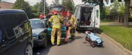 Strażacy z ratownikami medycznymi ewakuują kierowcą z pojazdu, po prawej tył karetki z otwartymi drzwiami 