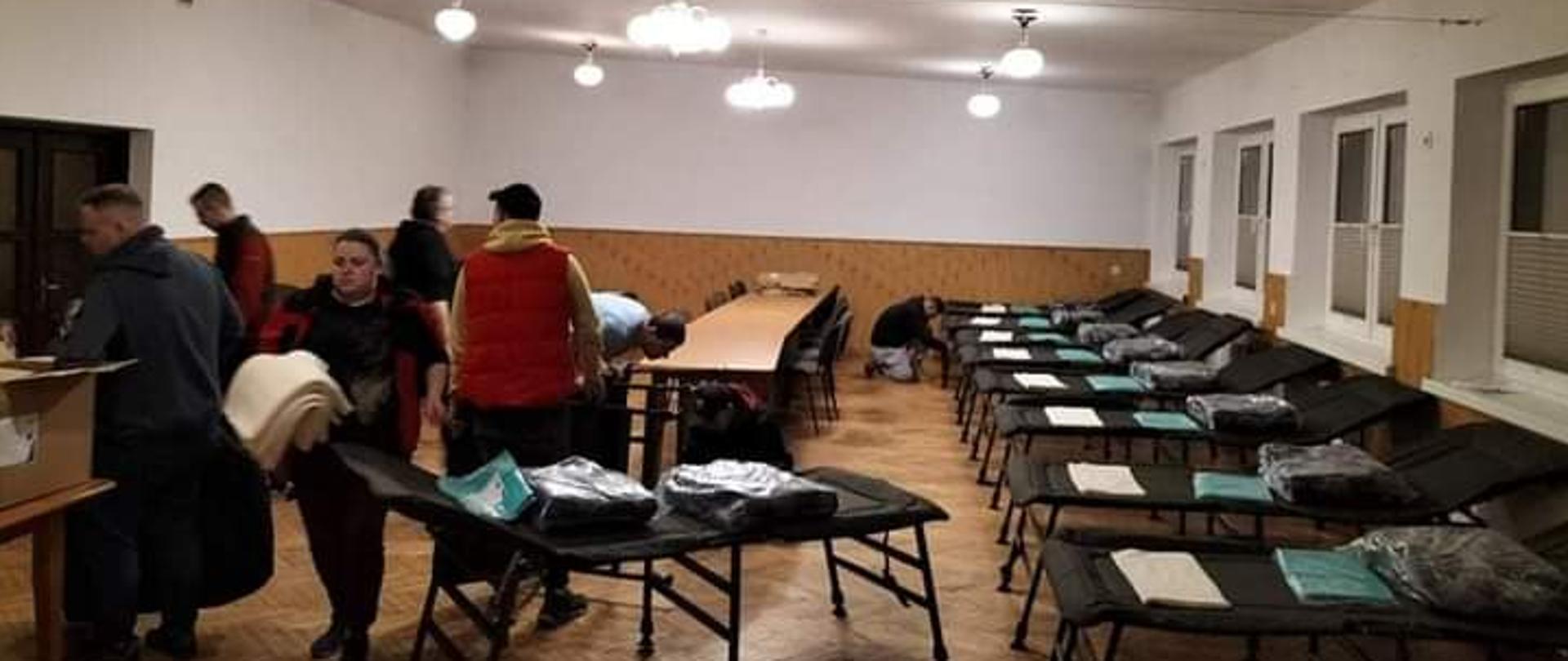 Na zdjęciu widoczne miejsca noclegowe przygotowane przez strażaków OSP między innymi łóżka polowe, stoliki, koce, rozłożone w remizie OSP w Bieczu na sali.