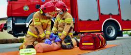 Strażacy przywracają czynności serca na tle samochodu gaśniczego.