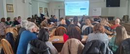 Przy stołach siedzi grupa osób i słucha wykładu o usłudze KSeF
