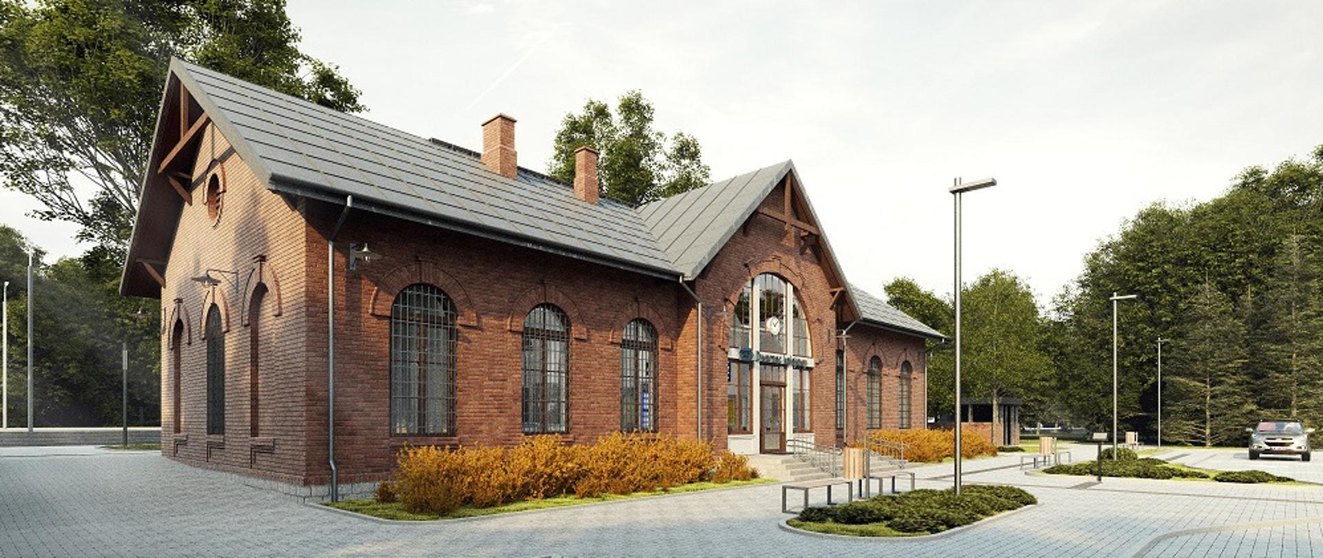 Na zdjęciu widoczny budynek dworca z czerwonej z cegły. Wokół równo ułożony chodnik, widoczne miejsca parkingowe.