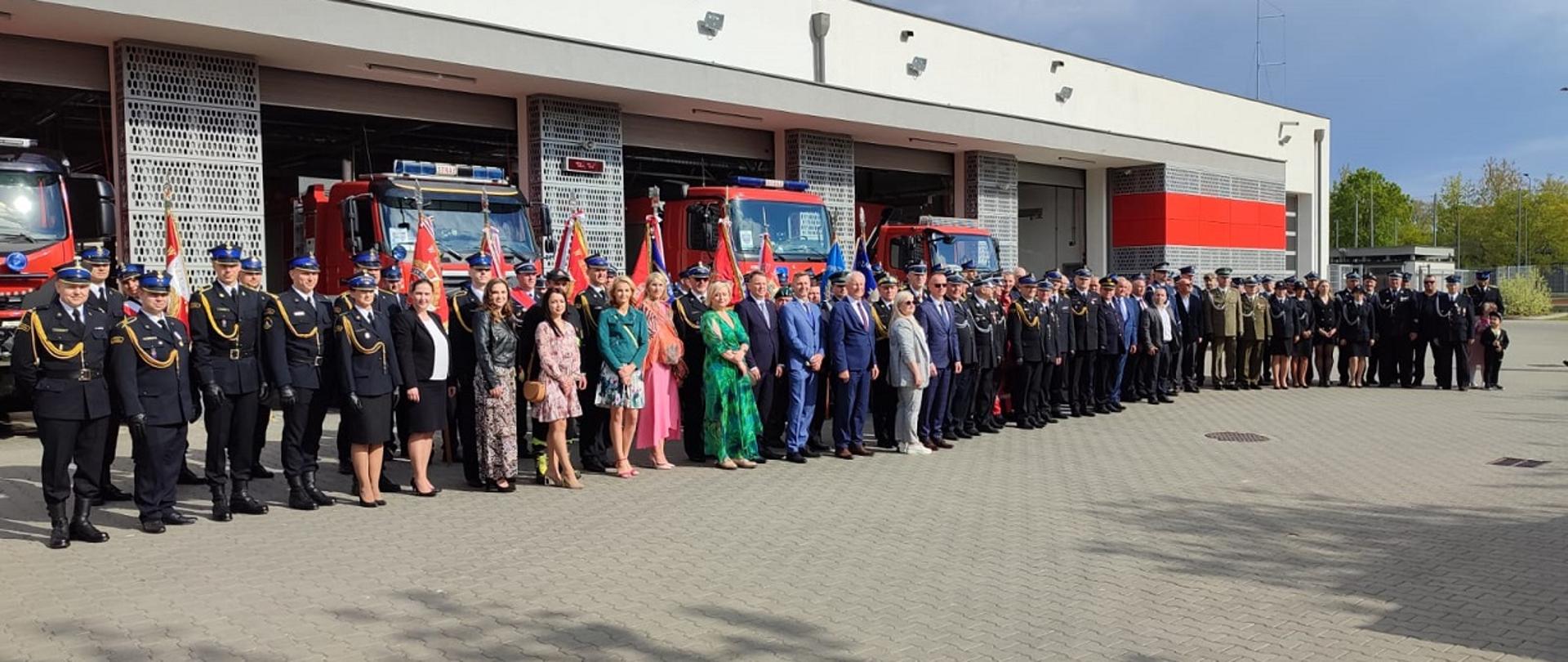 Strażacy i goście na tle garaży straży pożarnej