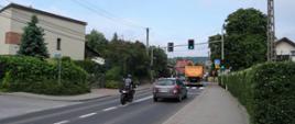 Zdjęcie przedstawia drogę jednopasmową po jednym pasie w każdym kierunku. Widoczne samochody i motocykl. 