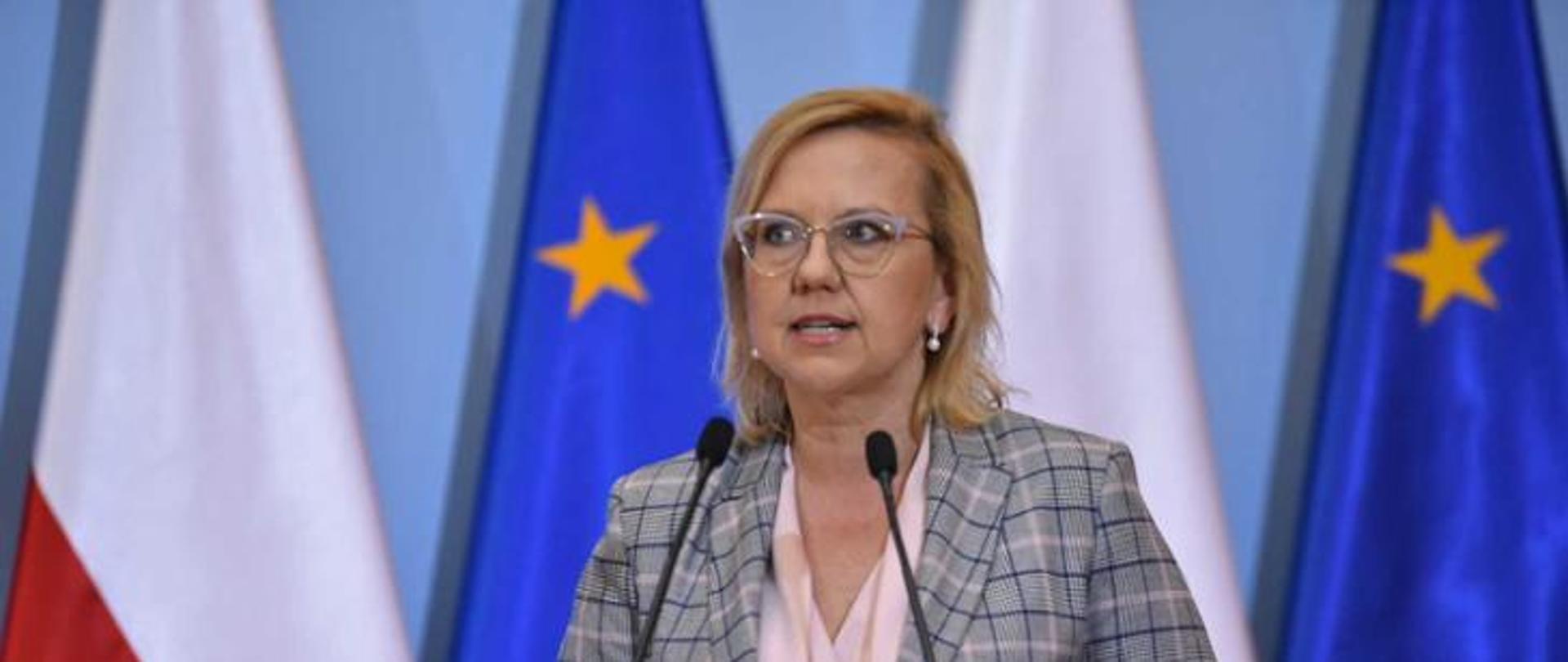 Jedna kobieta stojąca przed mównicą i wypowiadająca się 