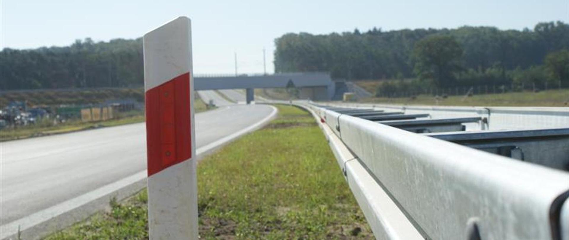 Widok na drogę szybkiego ruchu z poziomu ziemi, w tle wiadukt i las