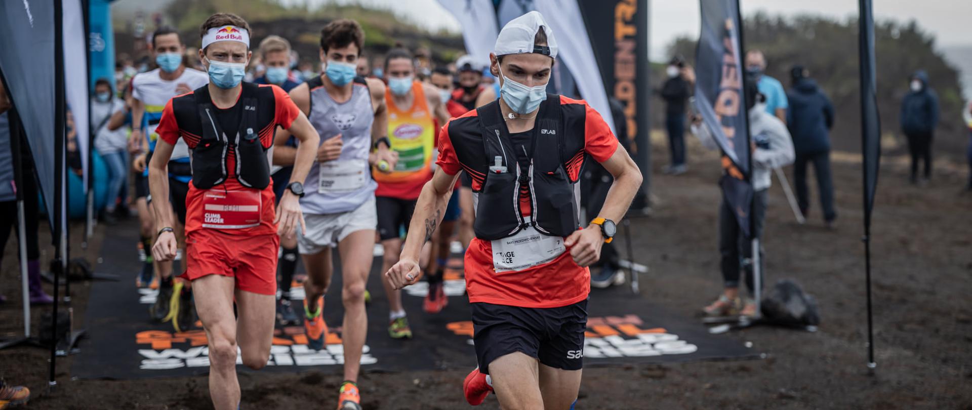 Biegacze w zwartej grupie tuż po starcie. Na twarzach mają maseczki. Na pierwszym planie Bartłomiej Przedwojewski.