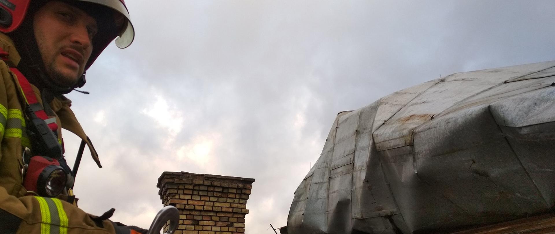 Zdjęcie obrazuje strażaka znajdującego się na uszkodzonym dachu