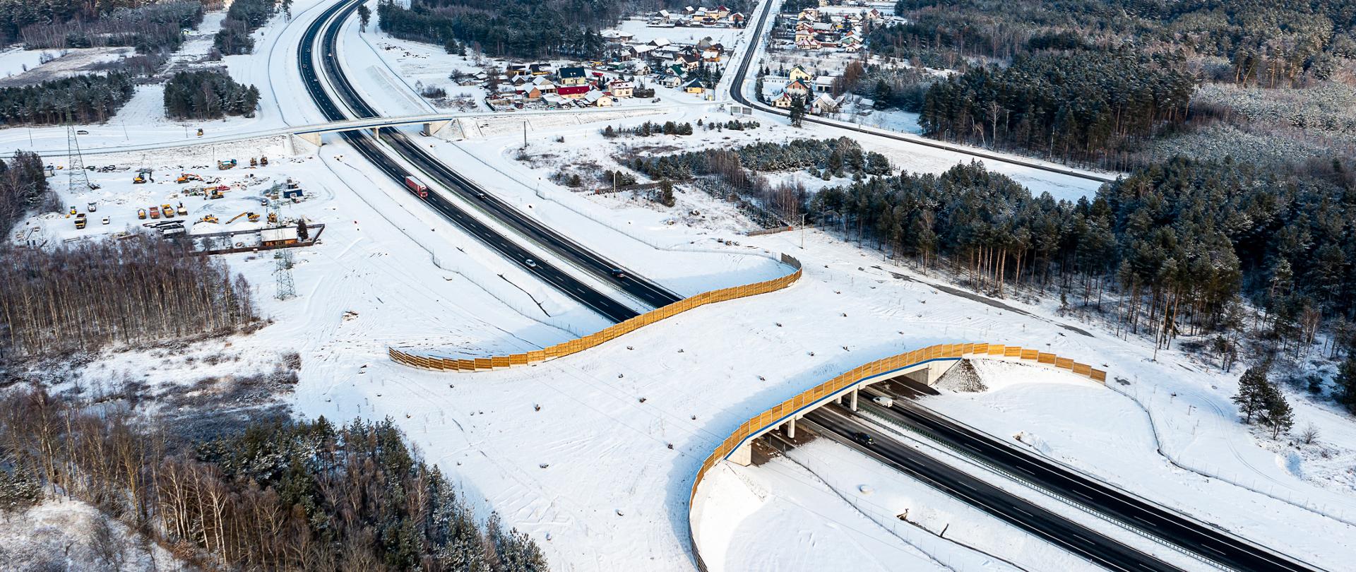 Zdjęcie z lotu ptaka w zimowej scenerii. Widać drogę S19 po dwa pasy ruchu w każdym kierunku. Na zdjęciu przejście dla zwierząt nad drogą w oddali wiadukt. Leży śnieg.