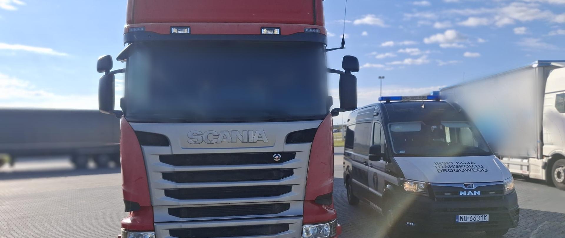 Czerwony ciągnik siodłowy Scania R450 zaparkowany na placu. Obok stoi oznakowany radiowóz Inspekcji Transportu Drogowego z niebieskimi światłami na dachu.