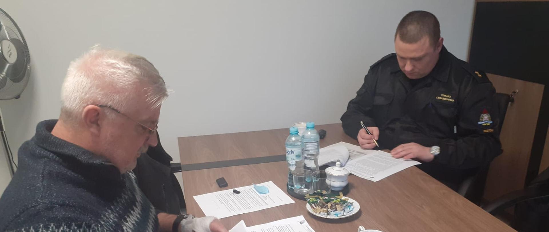 przy stole dwie osoby podpisują dokumenty