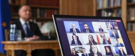 Na zdjęciu prezydent Duda podczas wideokonferencji, przed nim laptop na którym widać uczestników.
