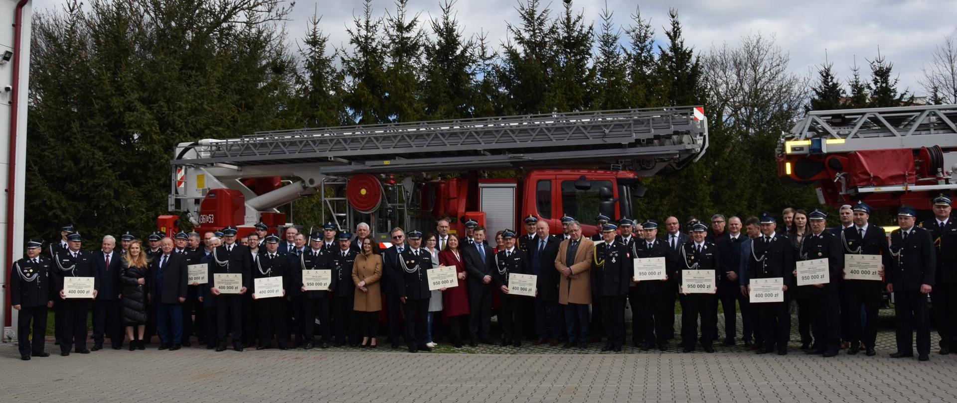 Na zdjęciu na tle samochodów pożarniczych przedstawiciele OSP oraz zaproszeni goście z wręczonymi podczas uroczystego apelu promesami