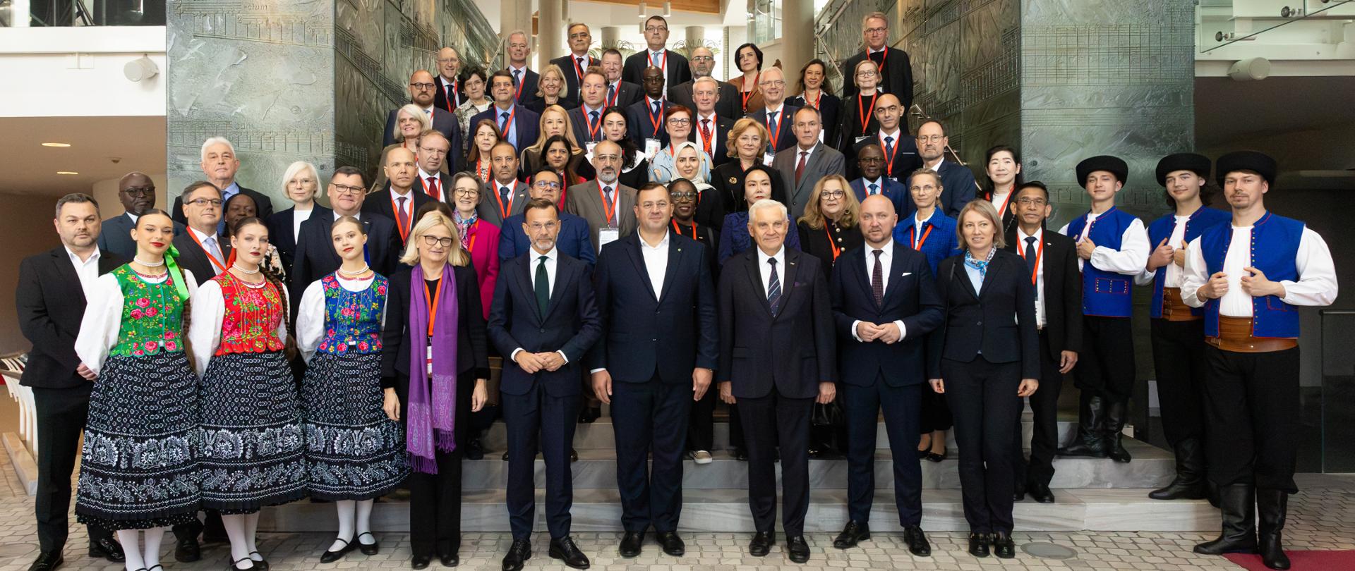 A photograph of a group of members of the Diplomatic Corps together with women and men in traditional Podlaskie costumes.