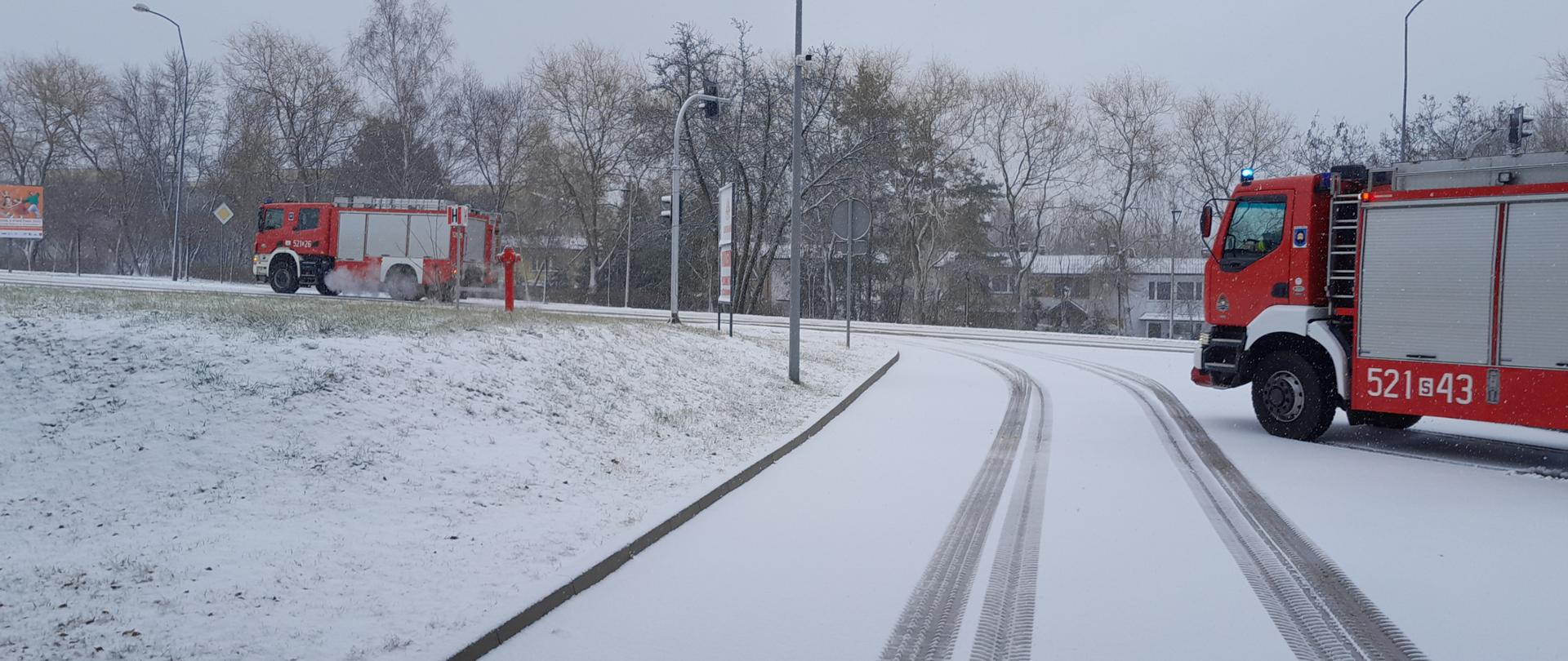 Zdjęcie przedstawia ośnieżony wyjazd ze strażnicy i wyjeżdżające samochody ratowniczo - gaśnicze do zdarzenia.
