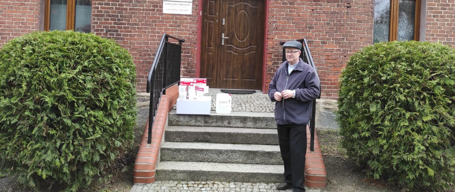 Na zdjęciu Ksiądz stojący obok wręczonych środków ochrony indywidulnej 