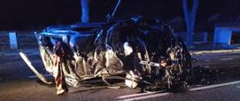 Zdjęcie przedstawia doszczętnie rozbity samochód osoby leżący na boku na pasie drogi.