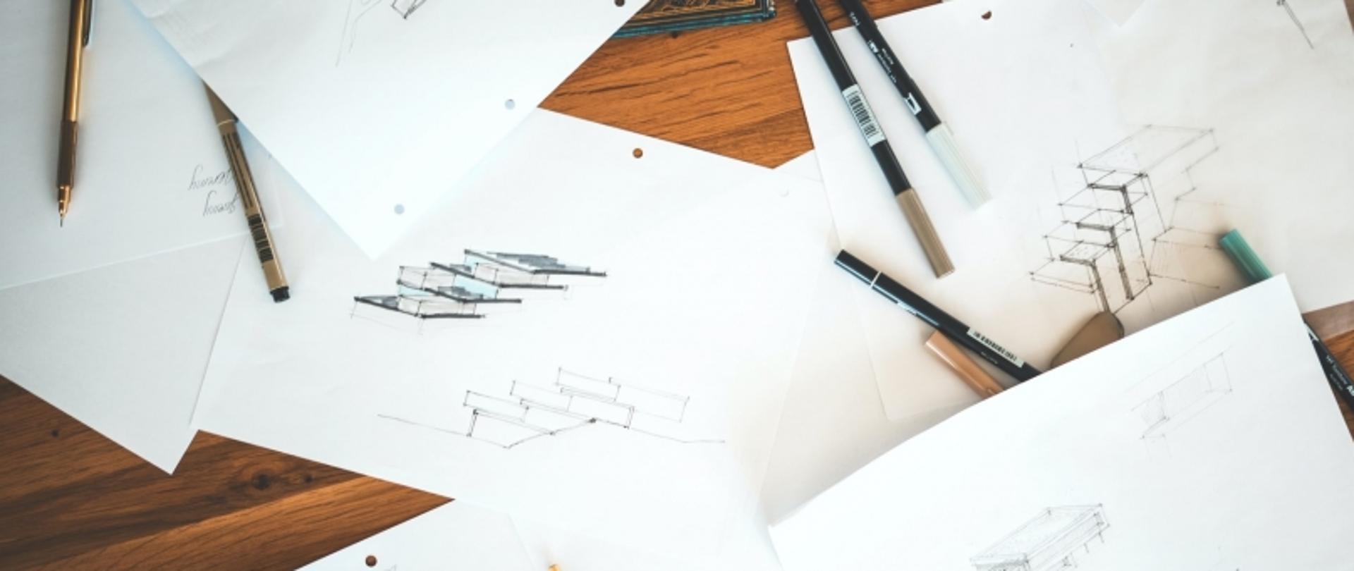 Stół z projektami architektonicznymi i przyborami do rysowania.