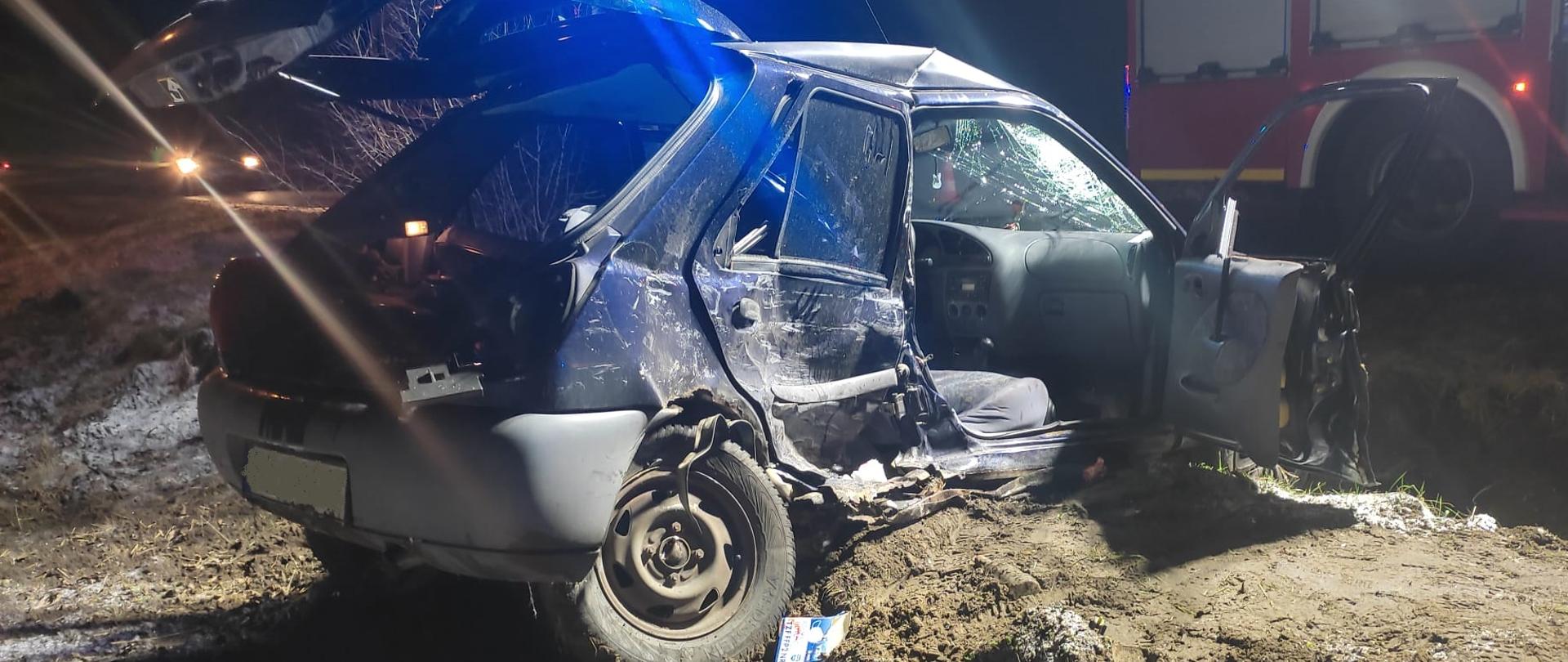 Zdjęcie przedstawia samochód osobowy znajdujący po wypadku. Samochód ma uszkodzony prawy bok.