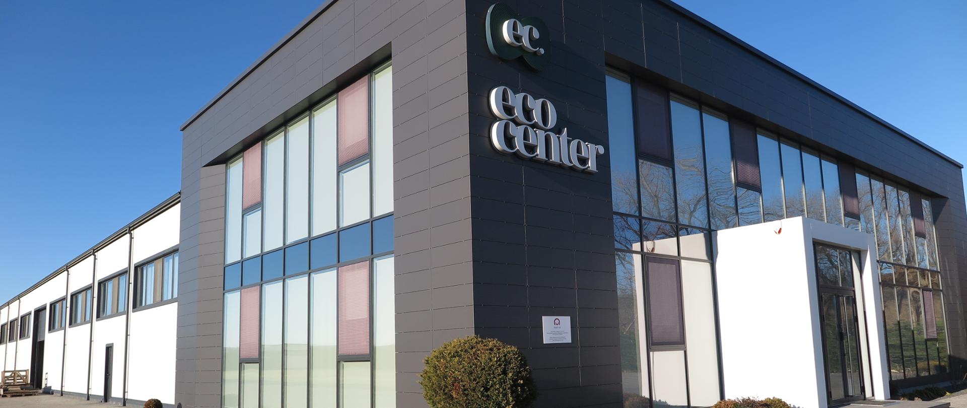 Budynek biurowy z napisem EcoCenter. Na budynku wisi niewielka tabliczka z logo Polskiej pomocy