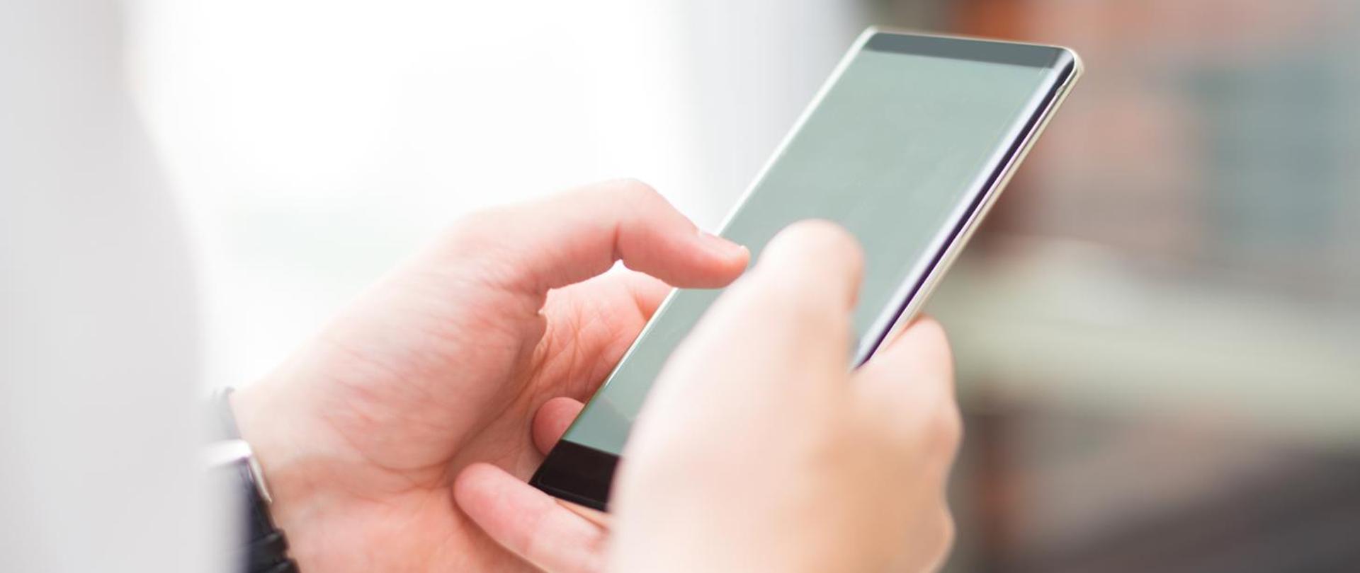 Dłonie trzymające smartfon i dotykające ekranu telefonu komórkowego.