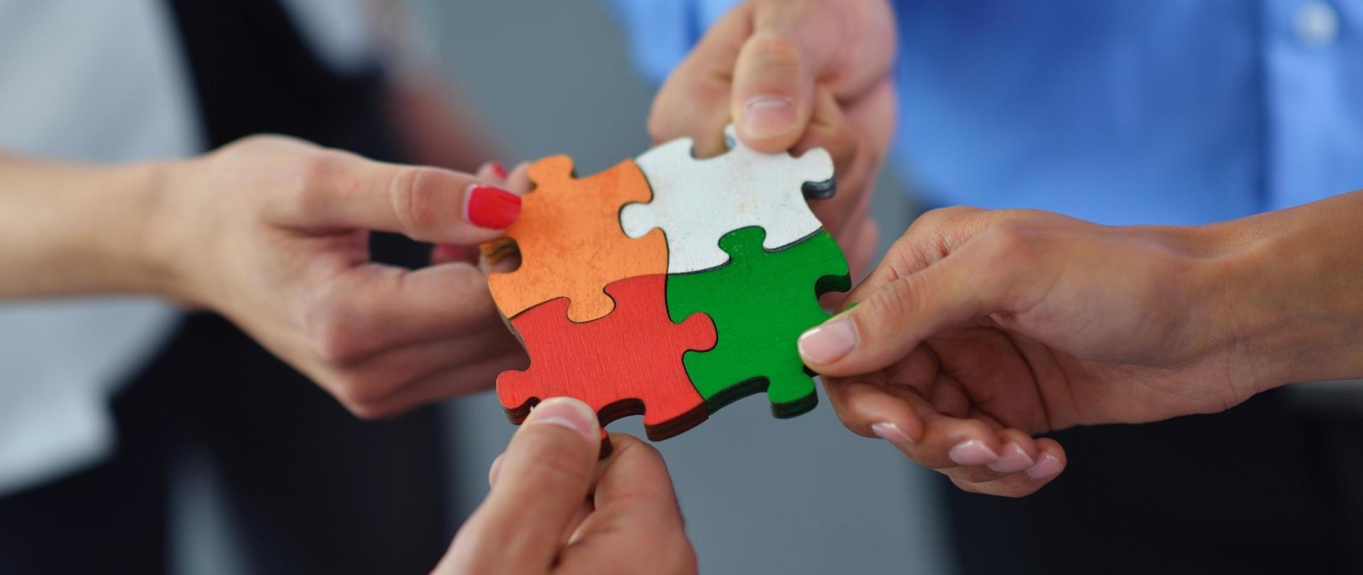 Cztery dłonie trzymające puzzle.