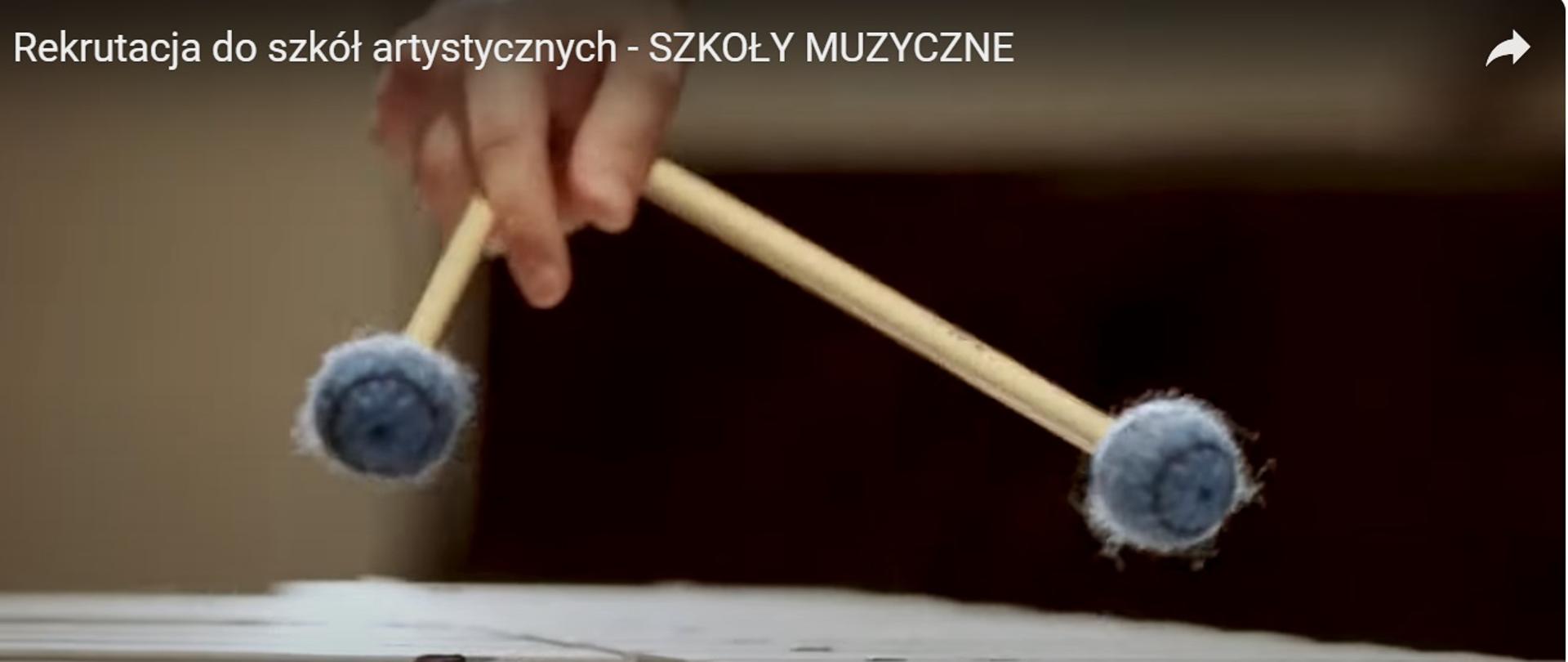 Grafika przedstawia fotografie dłoni trzymającej pałki bębnowe