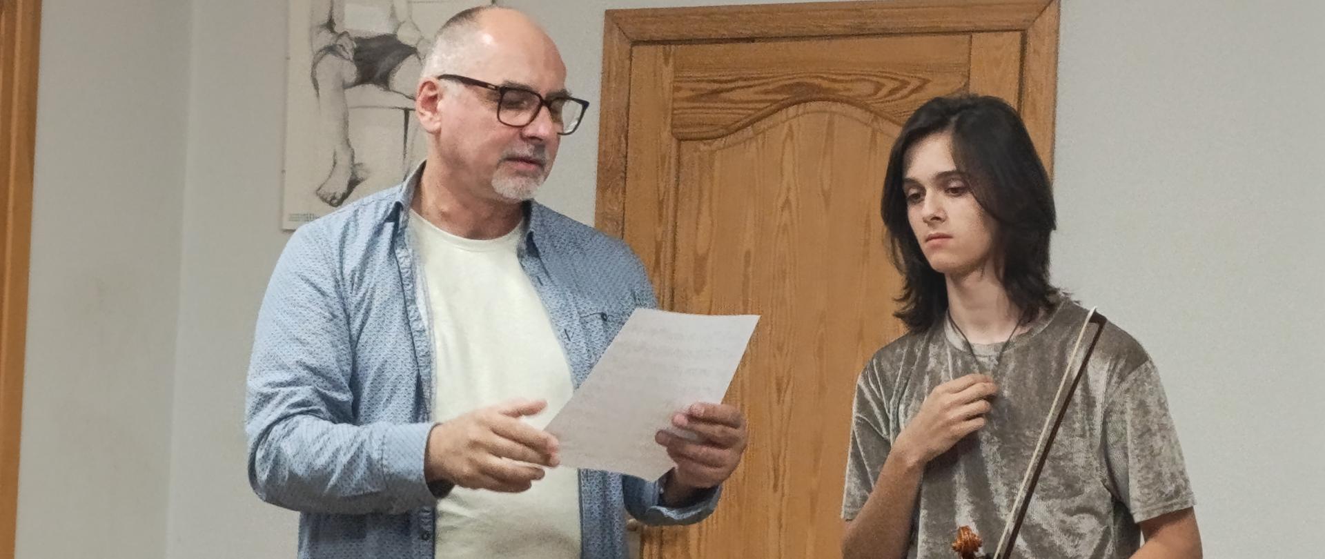 Bursowa świetlica. Po lewej stronie stoi pan Henryk Kacperczak, obok ze skrzypcami w ręku Staś, który wsłuchuje się w cenne wskazówki gry na skrzypcach.