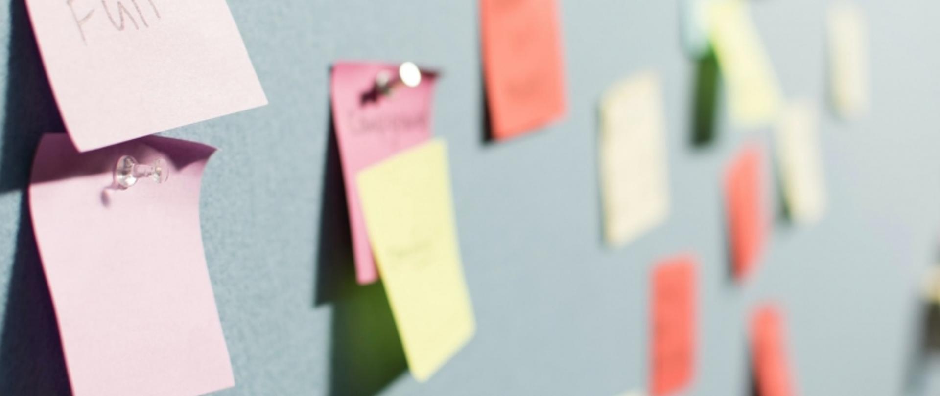 Tablica z wieloma kolorowymi karteczkami; część z nich zawiera nieczytelny tekst.