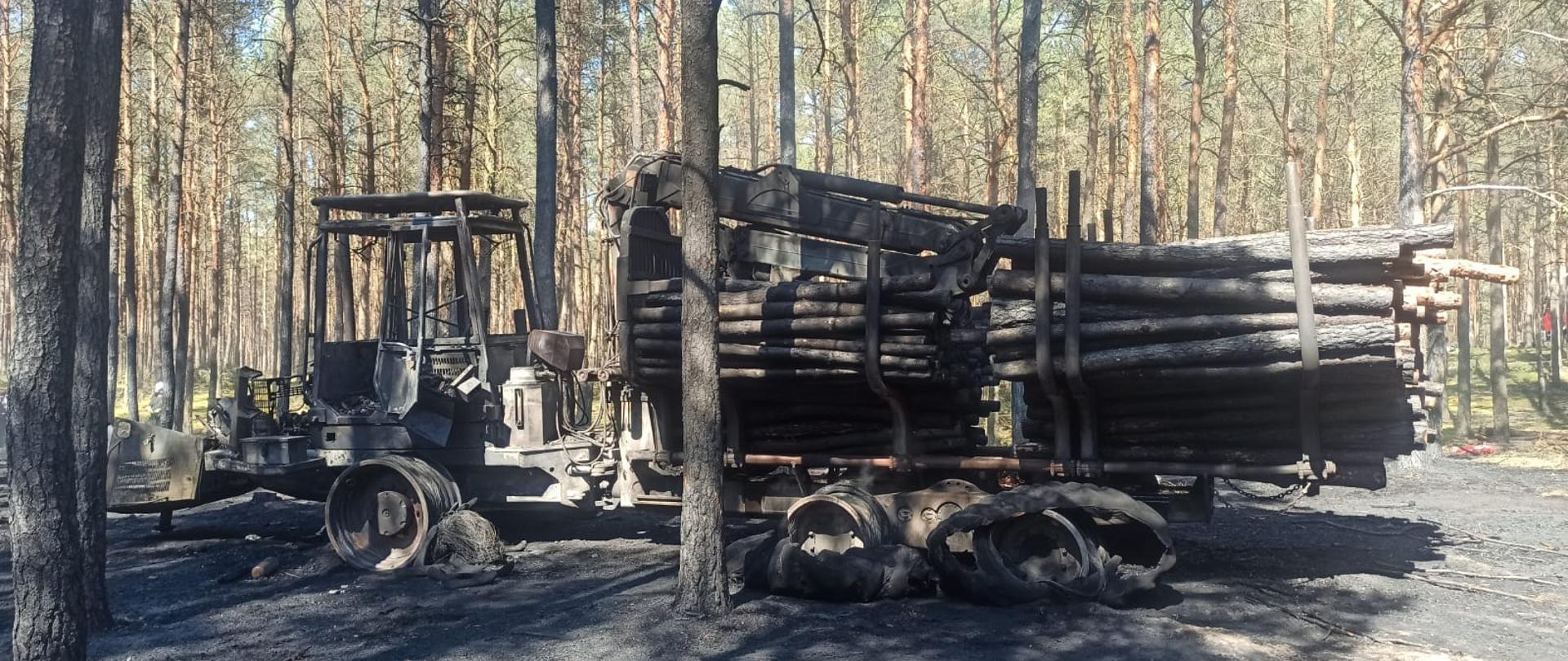 Widać spaloną maszynę do wycinki drzewa i poszycie leśne oraz przyczepę z drzewem