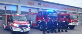 Minuta ciszy dla strażaka, który zmarł na służbie - na zdjęciu strażacy w ubraniu koszarowym na placu przed strażnicą na zbiórce w szeregu przed czerwonymi samochodami strażackimi.
