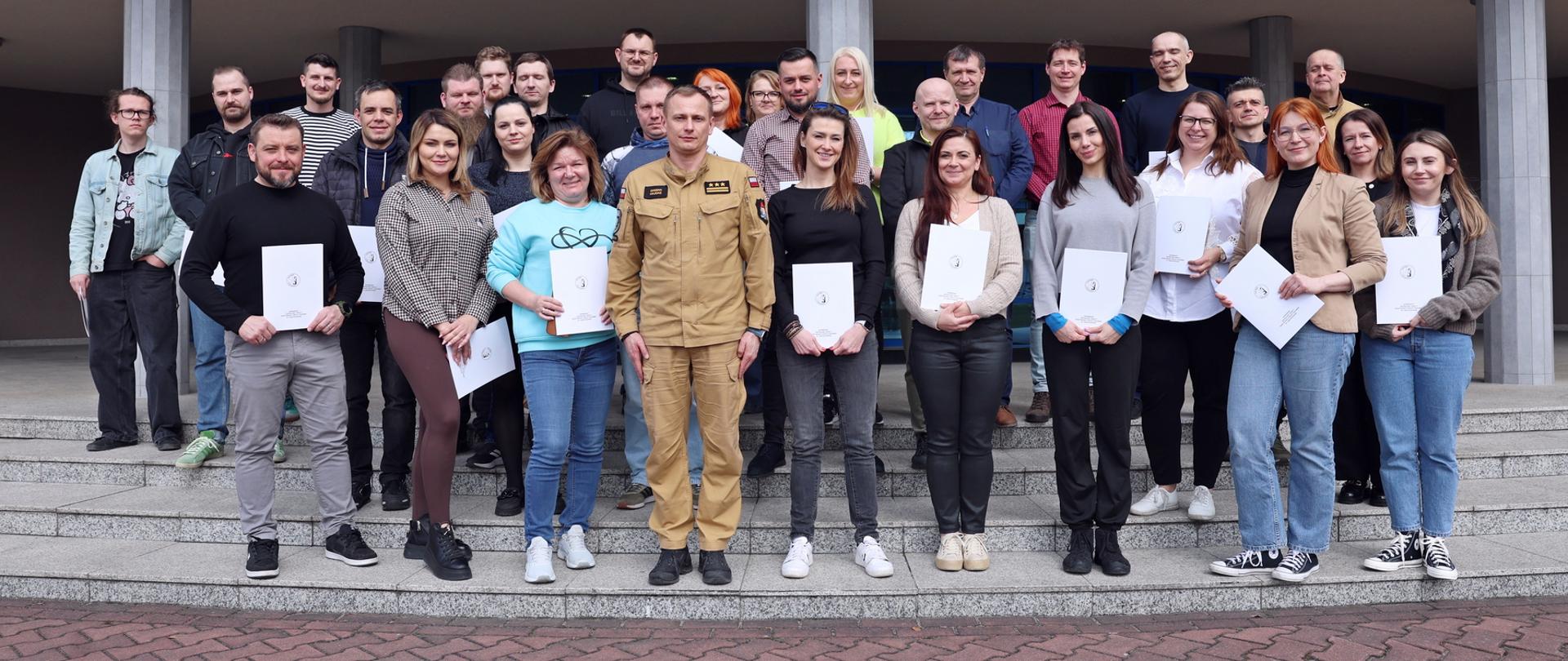 Pamiątkowe zdjęcie grupowe uczestników szkolenia inspektorów ochrony przeciwpożarowej (28 osób) w towarzystwie Zastępcy Komendanta Centralnej Szkoły PSP, kobiety oraz funkcjonariusza CS PSP
